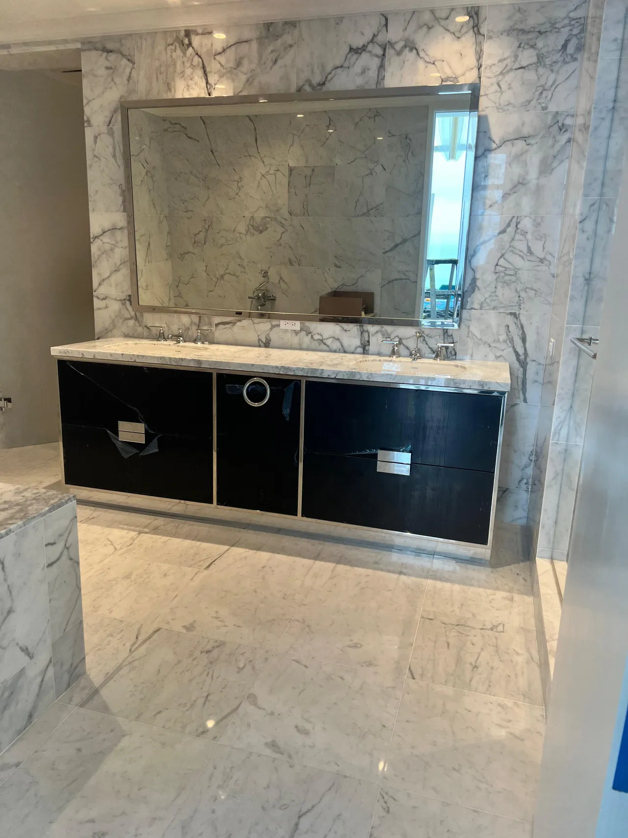 Black high-gloss floating double vanity with a white stone countertop and dual sinks, beneath a large chrome-framed mirror