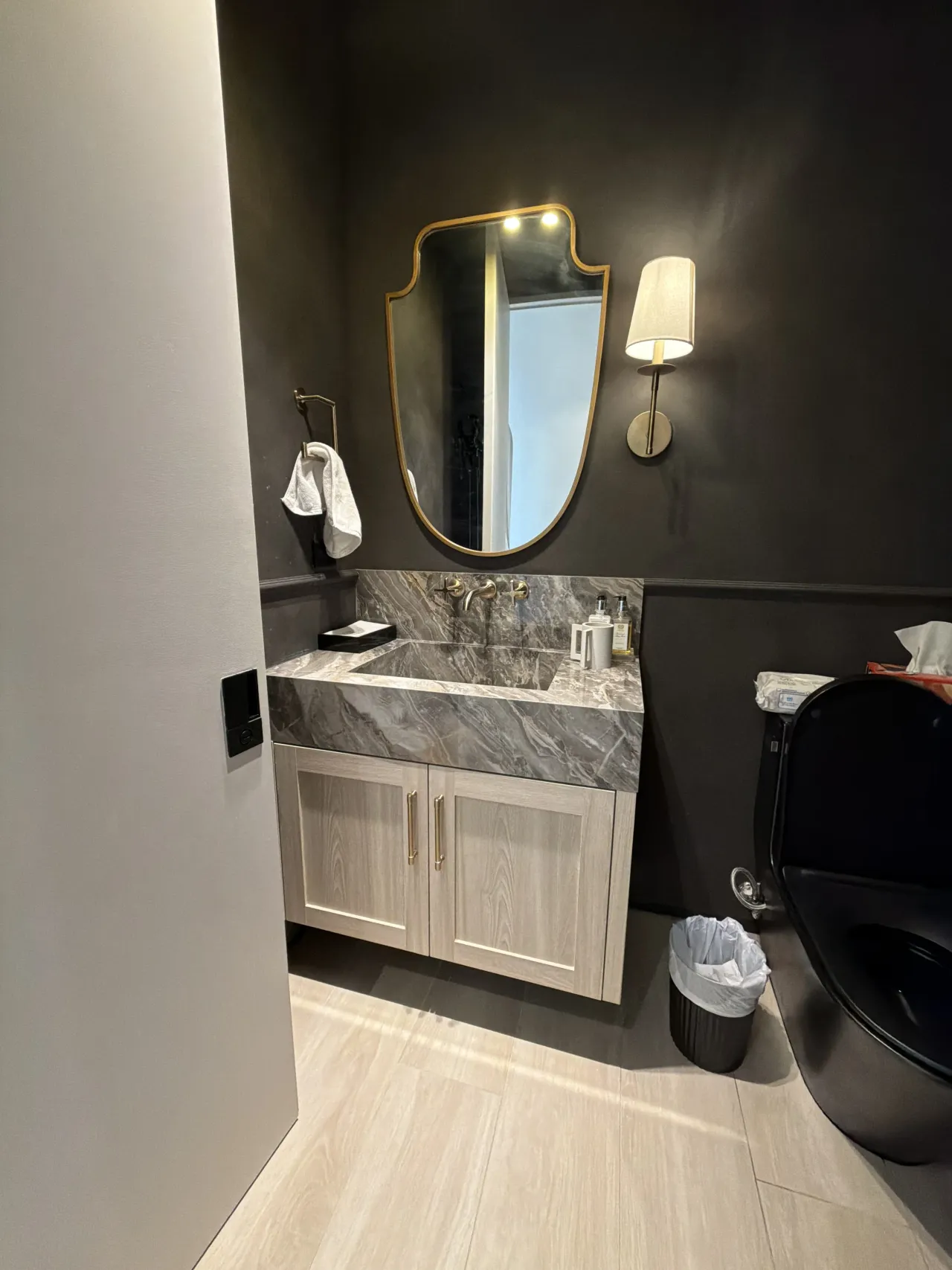Charcoal bathroom with an ornate gold-tone framed mirror, a gray-veined stone vanity top on a wood-grain cabinet, and a black toilet