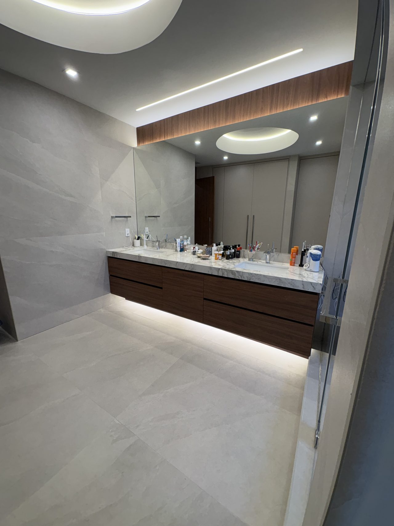 Dark wood-grain melamine floating double vanity with a light stone counter, a wide frameless mirror, and a wood-grain ceiling soffit