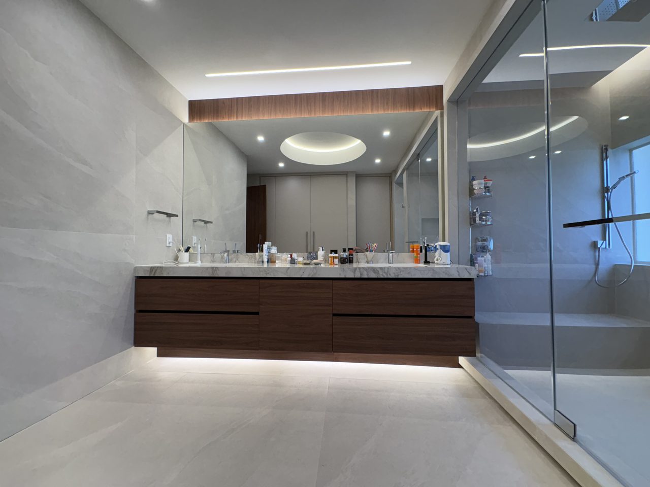 Dark wood-grain melamine floating vanity with a glass shower to the right showing a wall-mounted shower shelf caddy