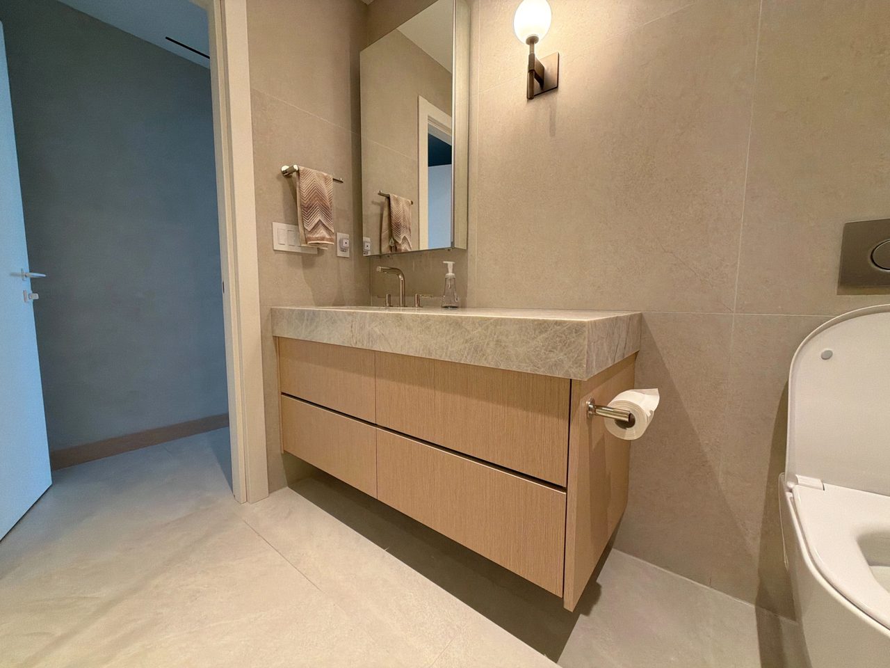 Floating custom-stained wood veneer vanity with four drawers, a veined stone top with integrated sink, framed mirror and a wall-hung toilet