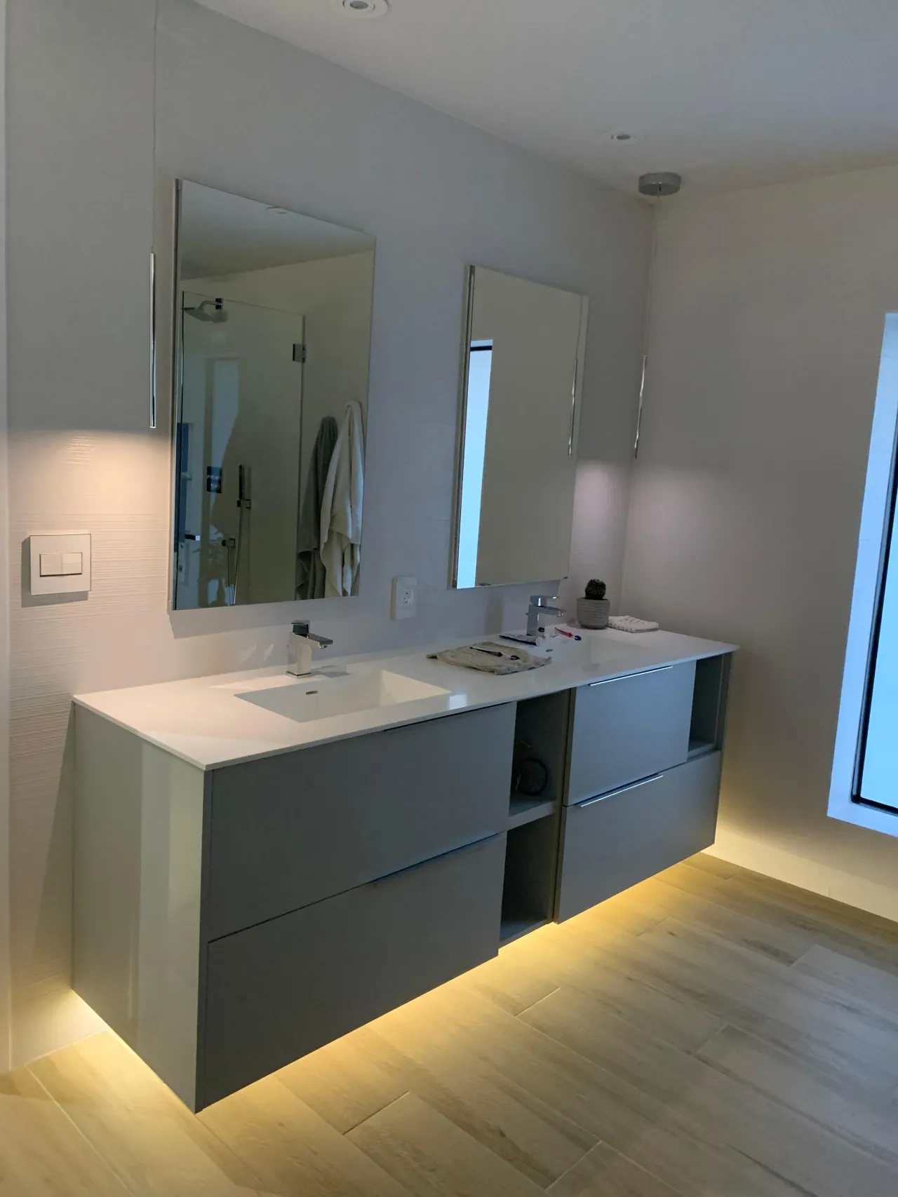 Gray floating double vanity with an open shelf cubby between the drawer sections, two mirrored medicine cabinets, and LED underlighting