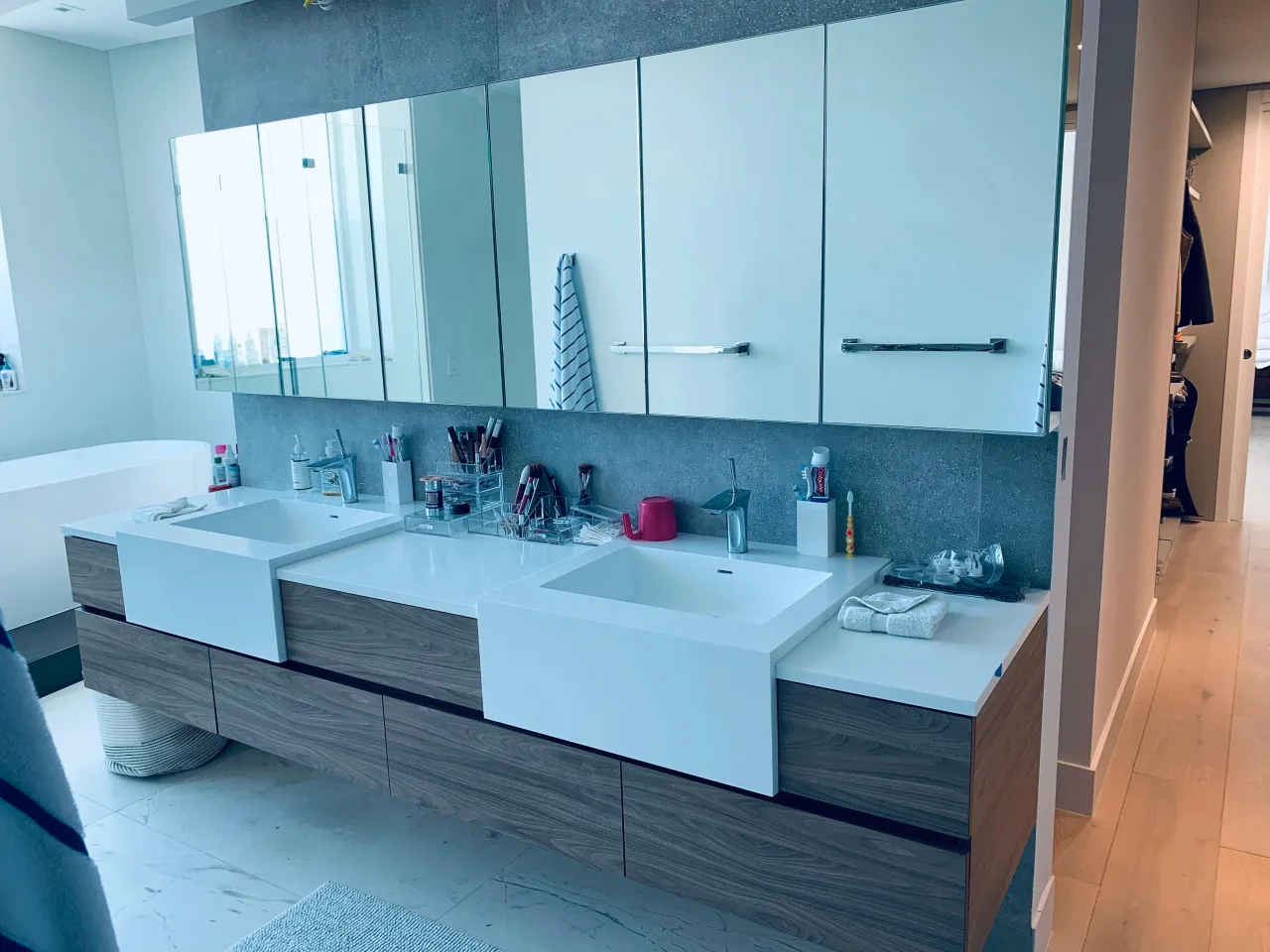 Gray wood-grain floating double vanity with two square white sinks, a gray stone backsplash, and a long run of mirrored and white wall cabinets