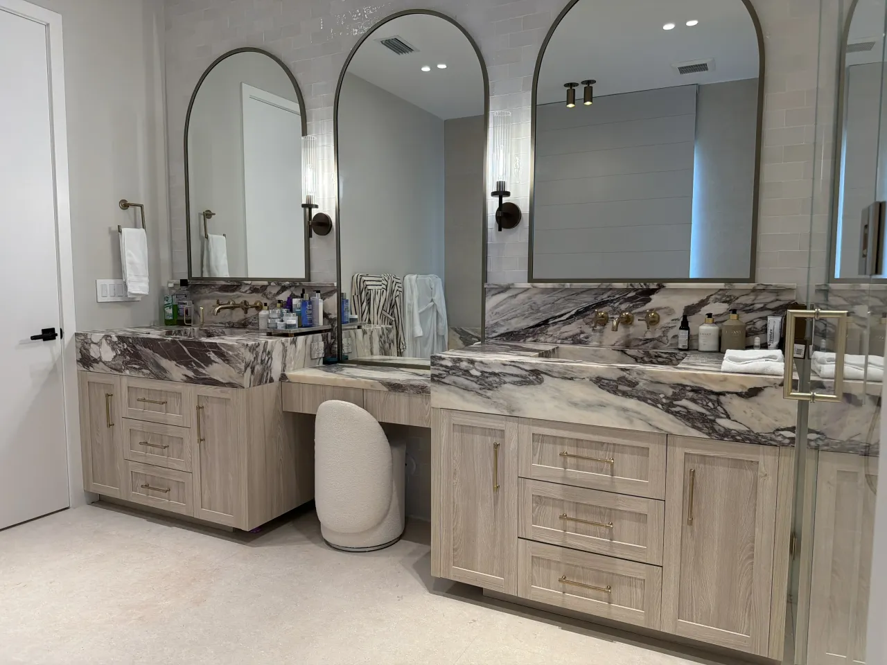 Light wood-grain melamine double vanity with triple arched mirrors and dark stone counters