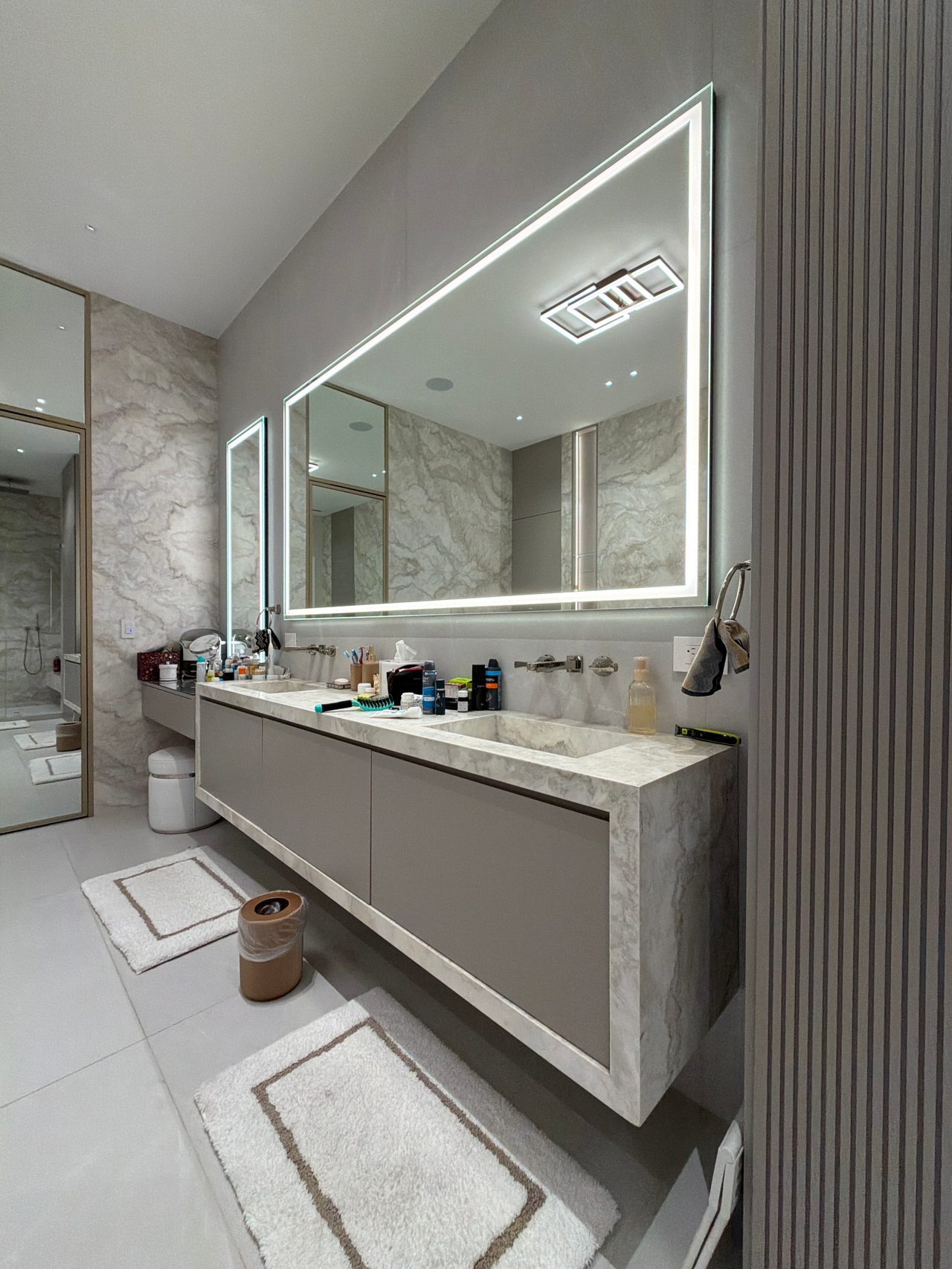 Stone-slab vanity top with taupe cabinet drawers, an illuminated rectangular LED mirror, and a stone slab wall reflected in the mirror