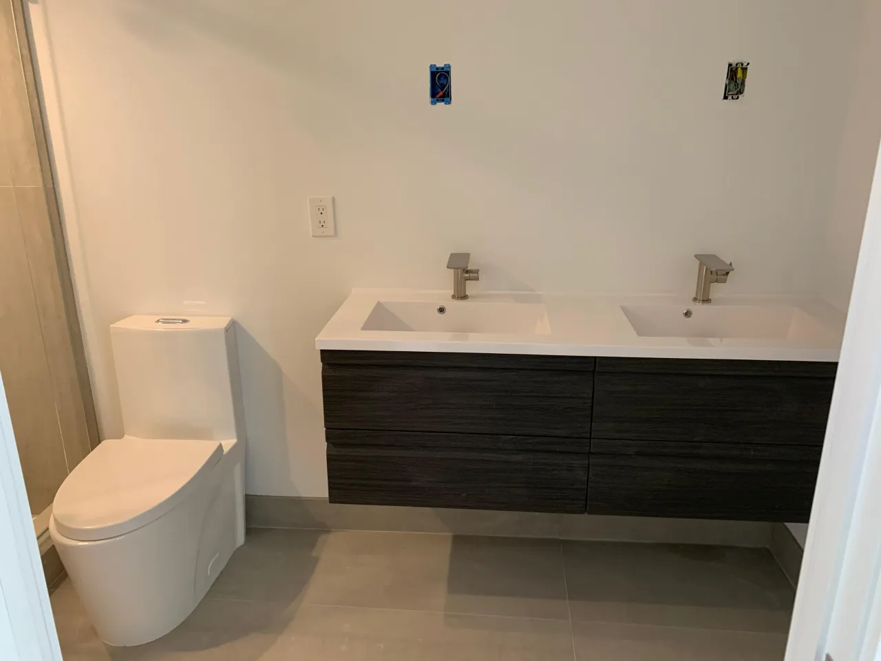 Unfinished bathroom with a dark wood double vanity cabinet and a molded white sink top, plus a toilet and shower stall, walls not yet painted