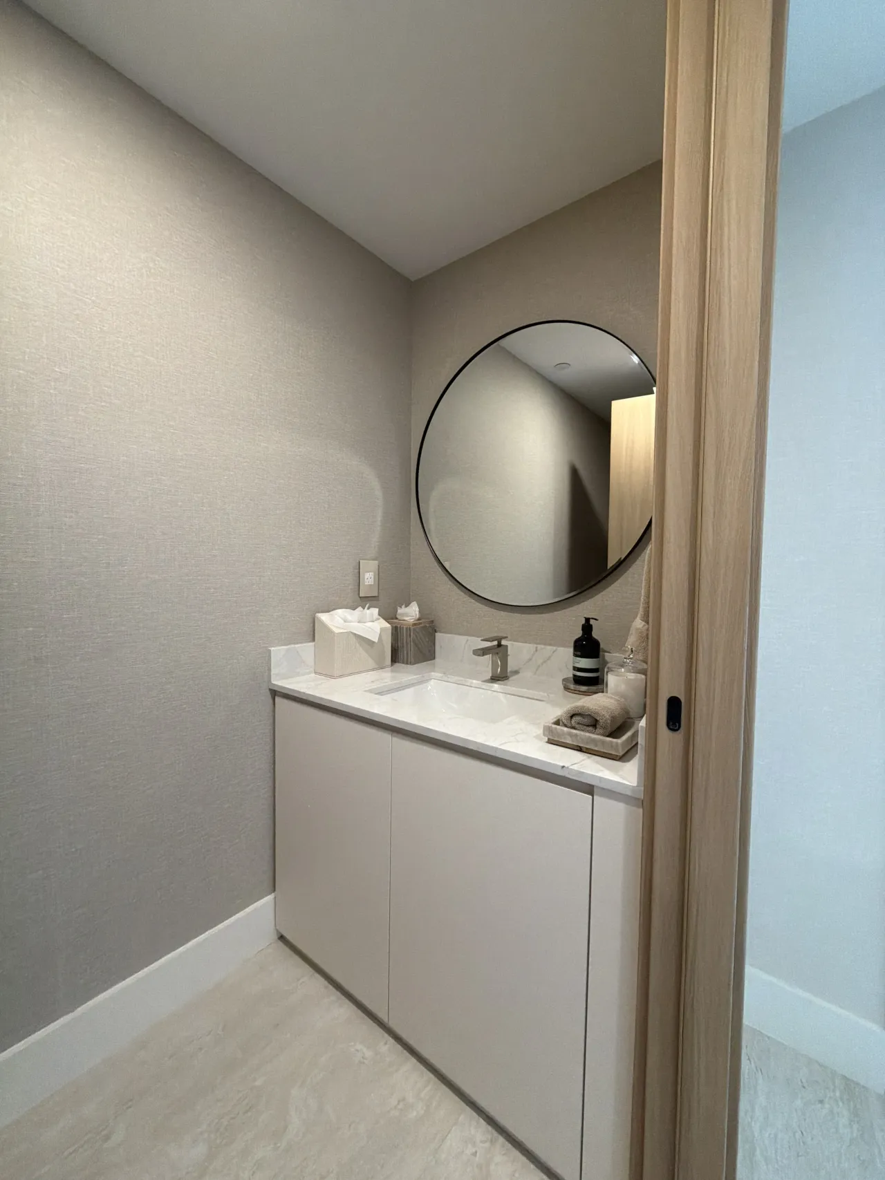 Small vanity nook with a round black-framed mirror over a white stone countertop and a beige flat-panel cabinet base