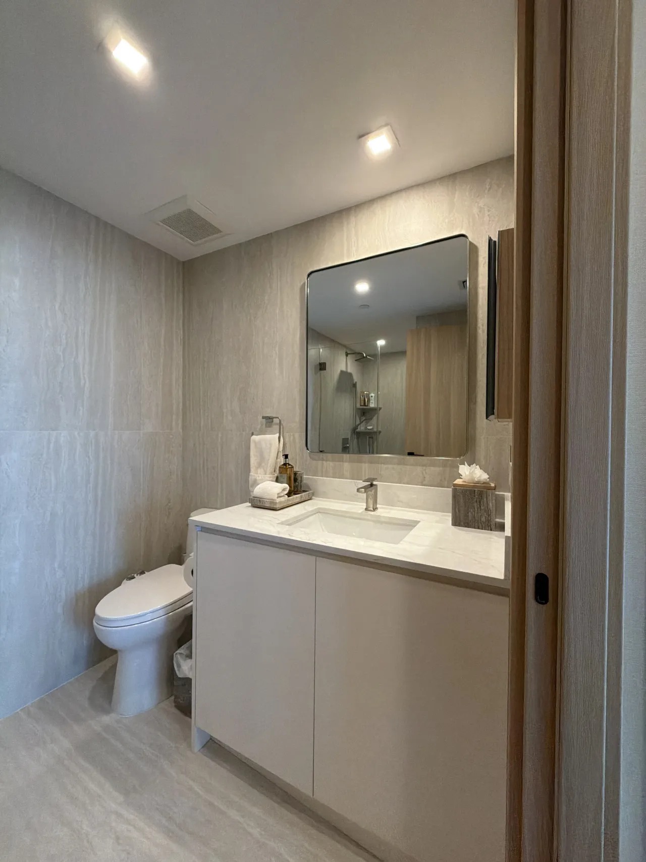 Bathroom vanity with white flat-panel cabinets, a white stone countertop, and a rounded-corner square mirror over stone-look tile walls