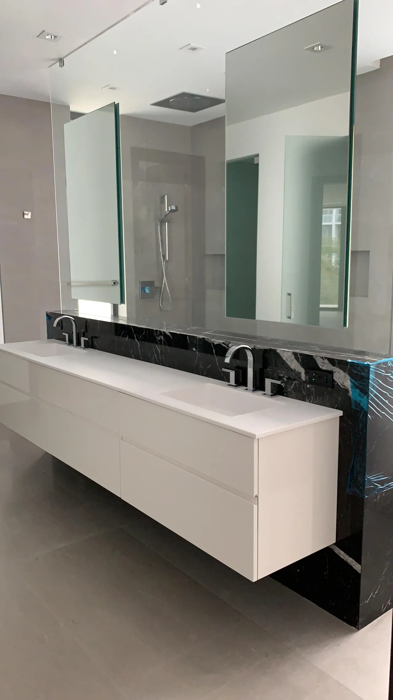 White floating double vanity with a white slab top against a black stone wall with white veining, under tall frameless mirror panels