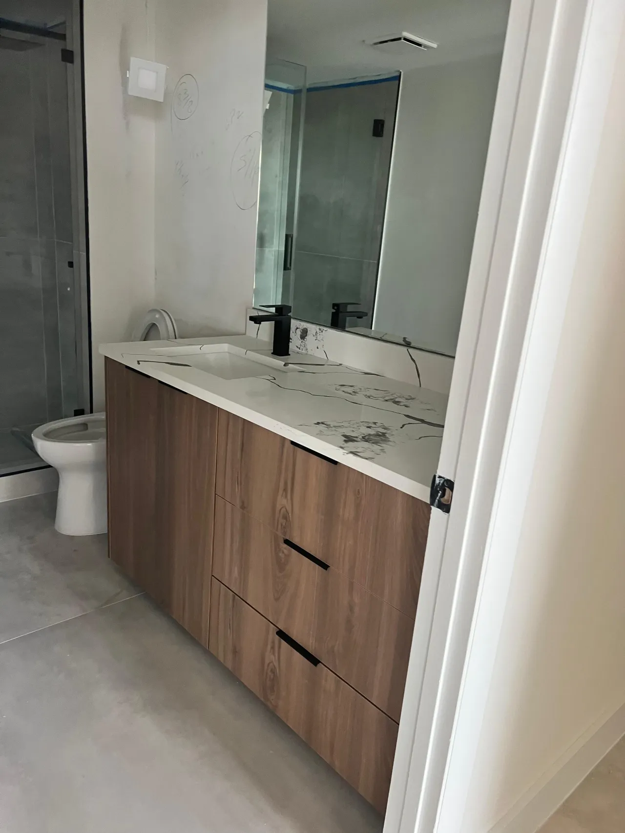 Wood-grain vanity with an undermount sink, a white countertop with black veining, and a matte black faucet and bar pulls
