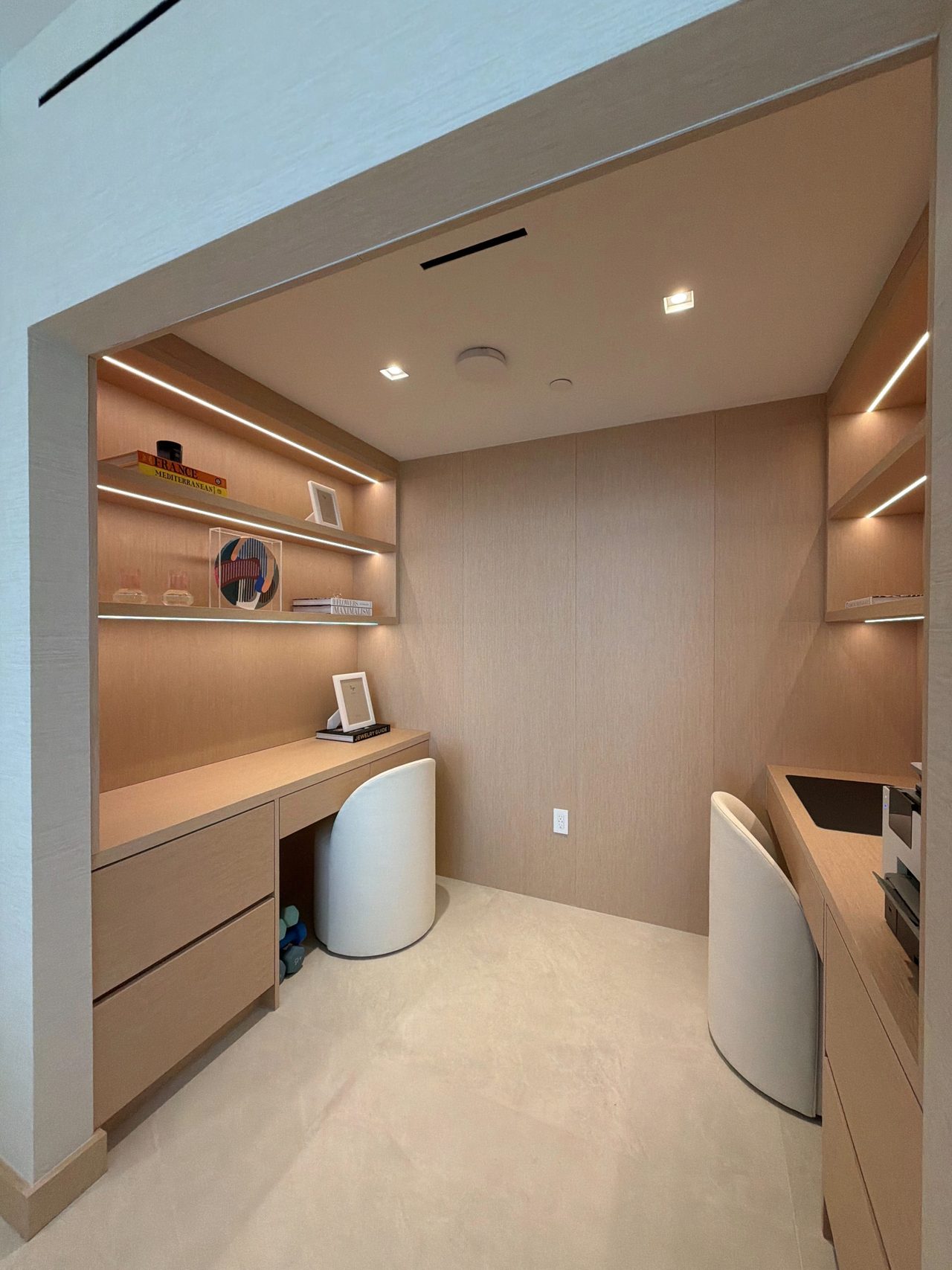Built-in office nook in custom-stained wood veneer with two desks, drawer banks, and integrated-LED floating shelves on both walls