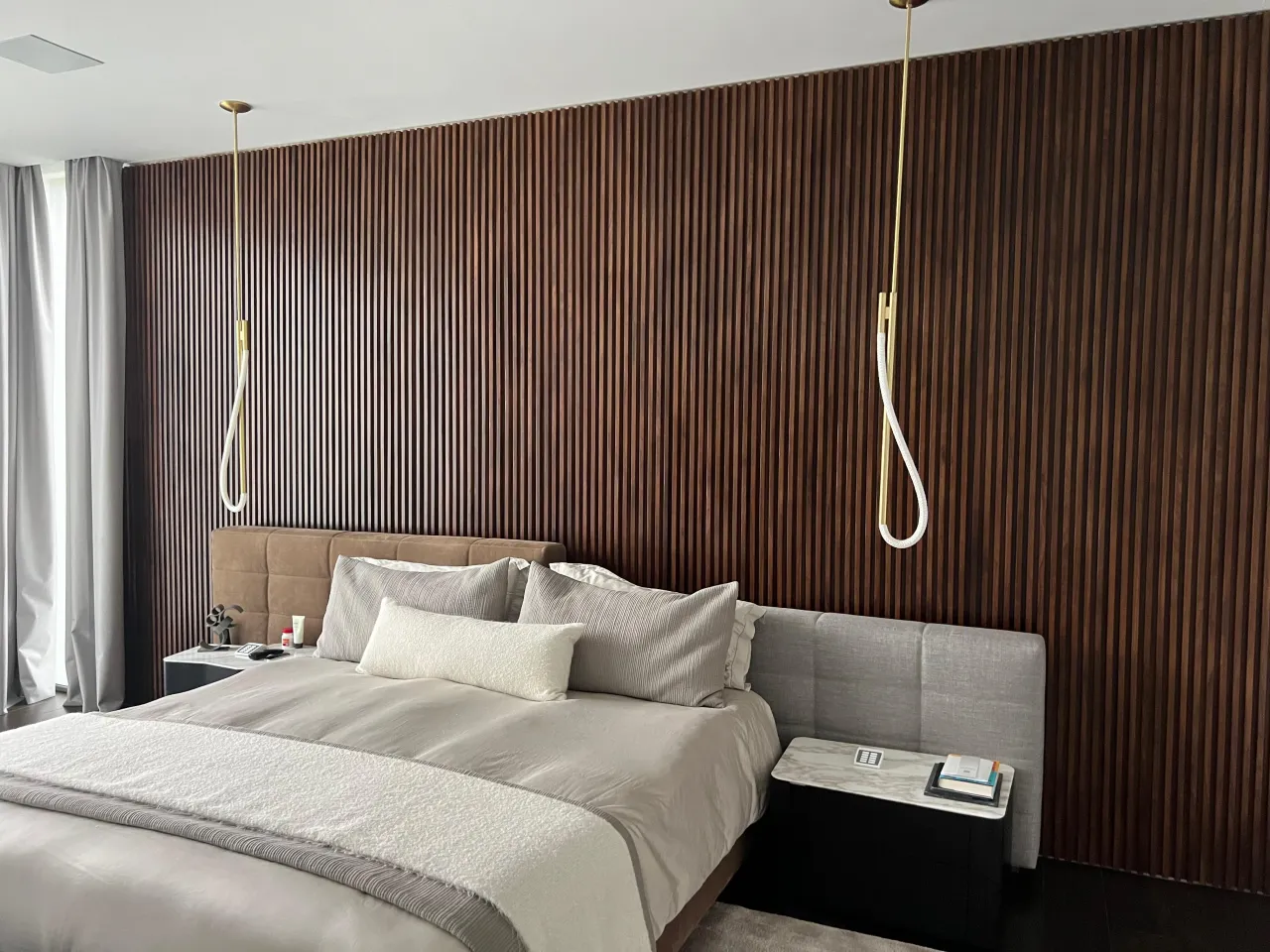 Bedroom with a full-height dark wood fluted slat accent wall behind an upholstered bed, two hanging pendant lights, and a nightstand