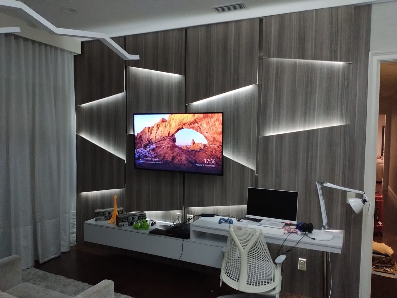 Living/media room with a dark wood panel wall featuring diagonal backlit LED cutouts surrounding a mounted TV