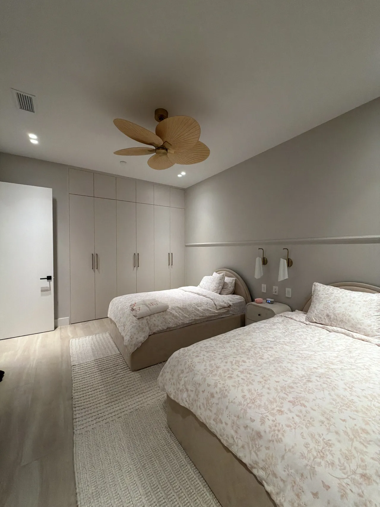 Twin bed room now with pink floral bedding, rattan ceiling fan and gray wainscoted walls