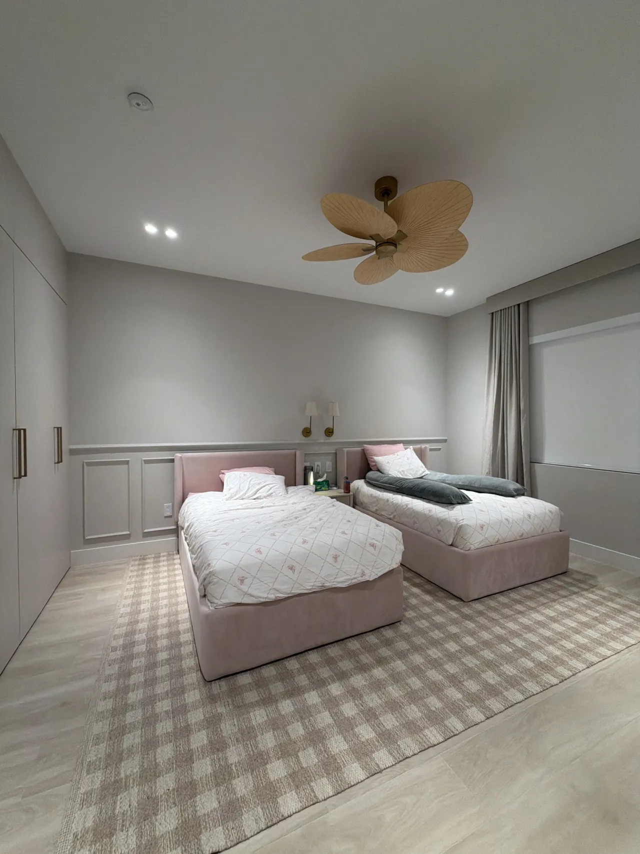 Twin beds upholstered in pink with a checked gingham rug beneath a rattan-blade ceiling fan