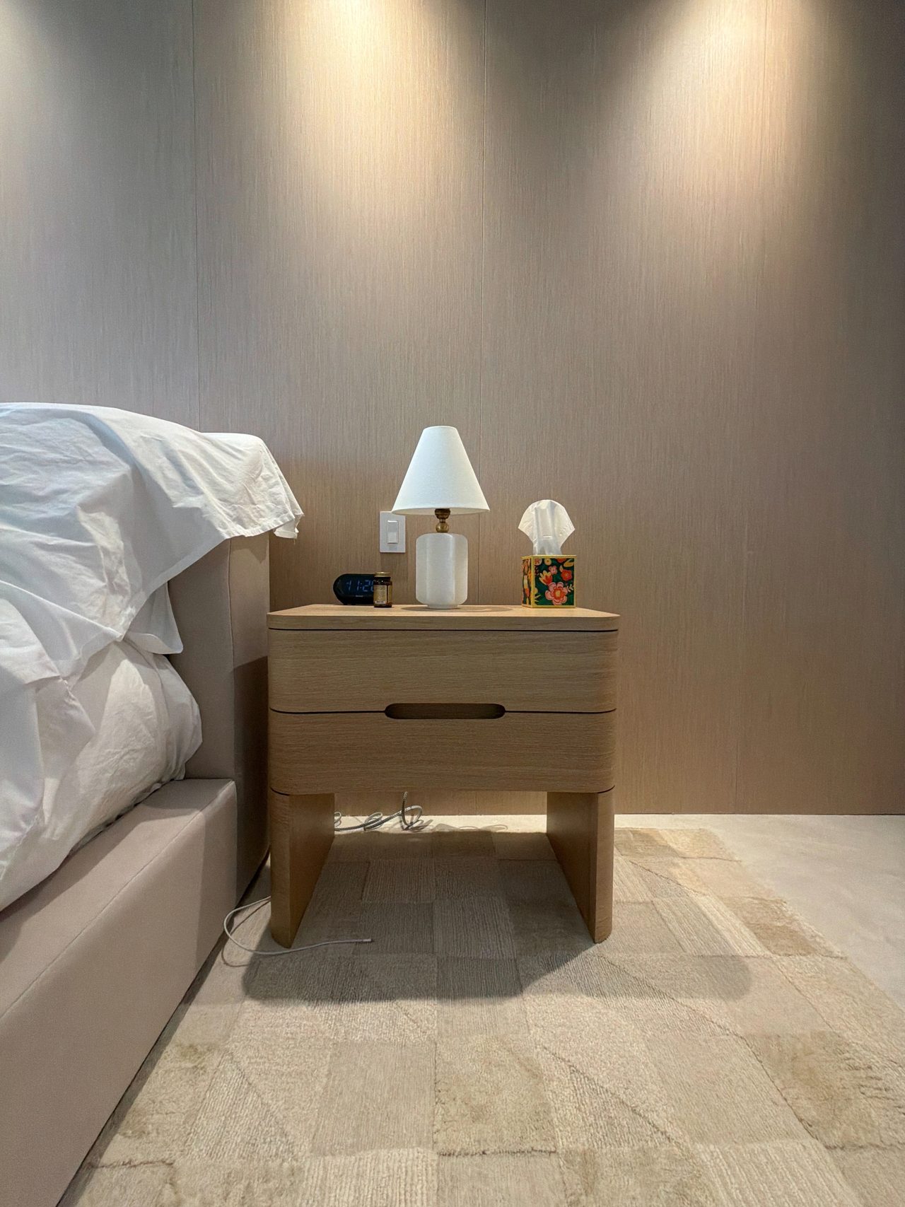 Two-drawer custom-stained wood veneer nightstand with rounded edges and recessed finger pulls beside an upholstered bed and a veneer wall