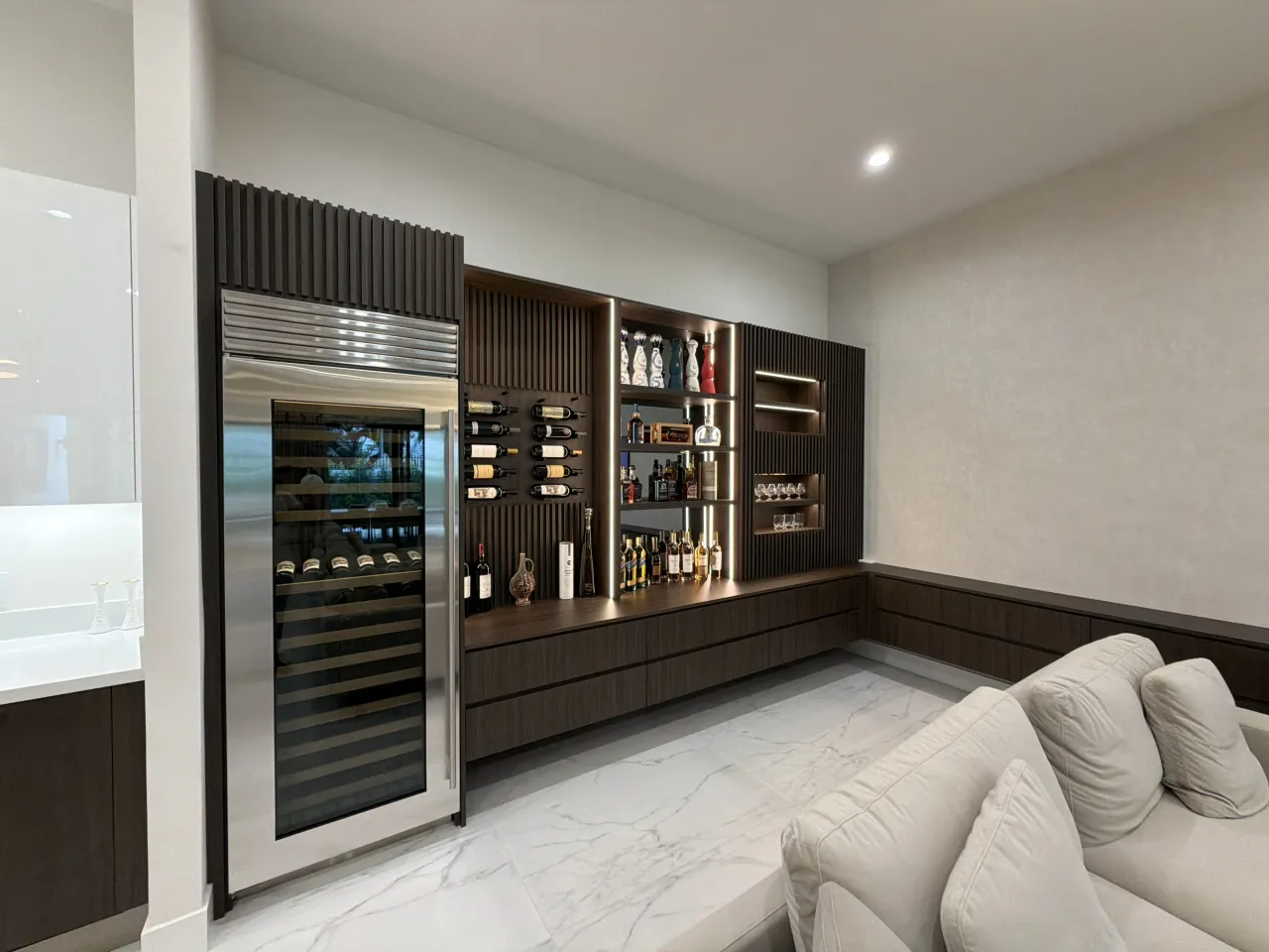 Built-in wine fridge and fluted dark wood-grain melamine wall with open bar shelving holding bottles and glassware