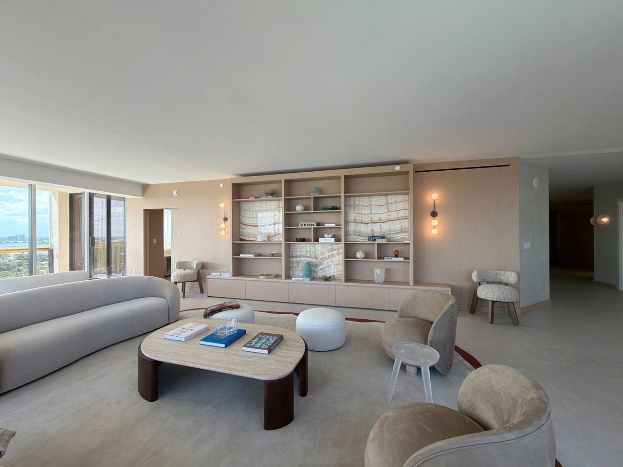 Custom-stained wood veneer built-in shelving wall with backlit veined-stone niches and a floating drawer base, in an open living area with a curved sofa