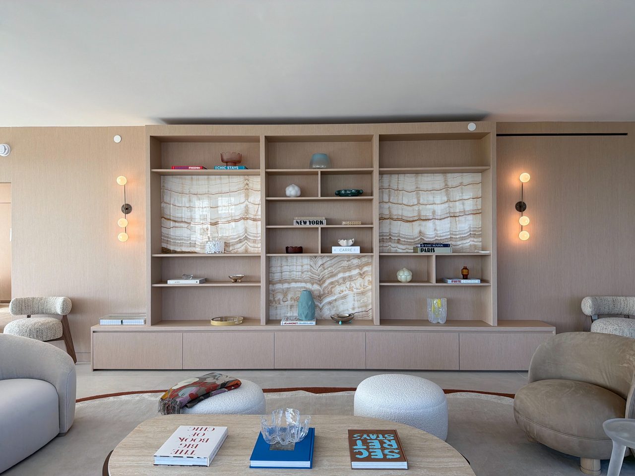 Close view of a custom-stained wood veneer built-in: open shelving, three book-matched backlit veined-stone panels, and a flush push-latch drawer base