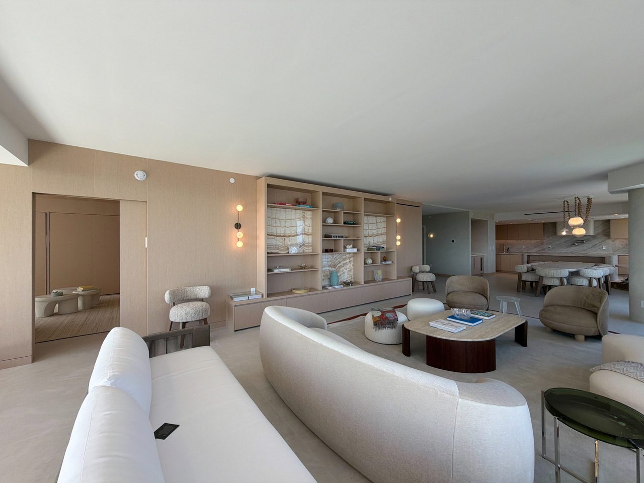 Custom-stained wood veneer built-in shelving wall with backlit veined-stone niches, viewed across a living area toward the kitchen and dining beyond