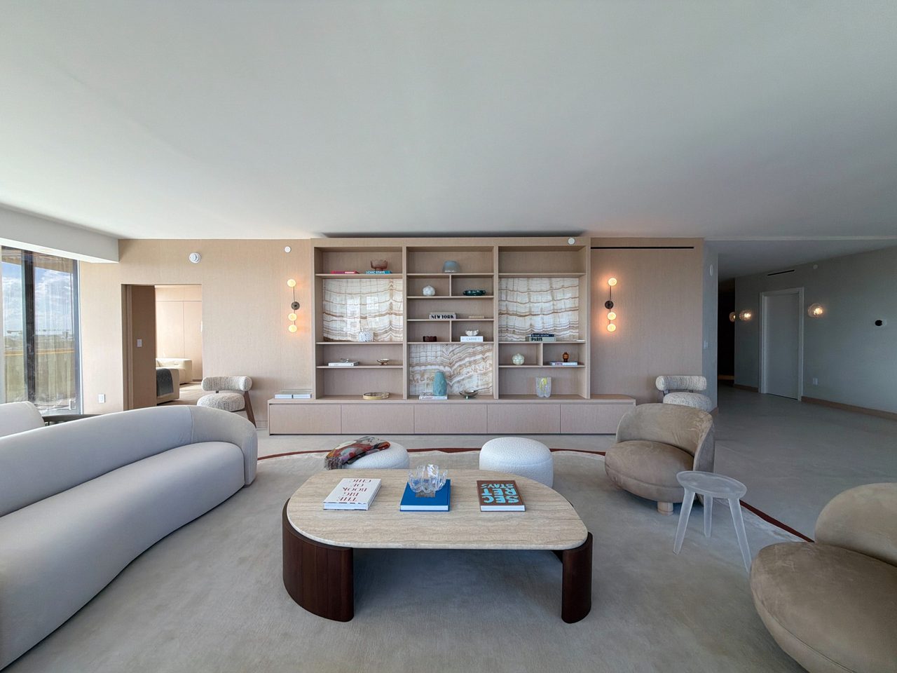 Custom-stained wood veneer built-in centered on a living area, with symmetrical open shelving, three backlit veined-stone niches, and a low credenza