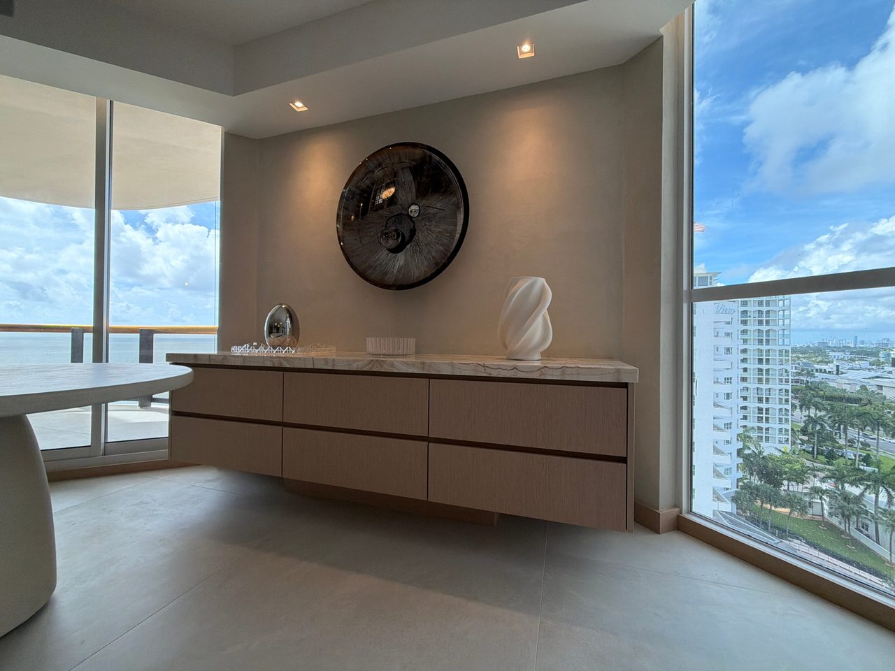 Low-angle view of a floating six-drawer credenza in custom-stained wood veneer with a veined stone top, under a round wall mirror