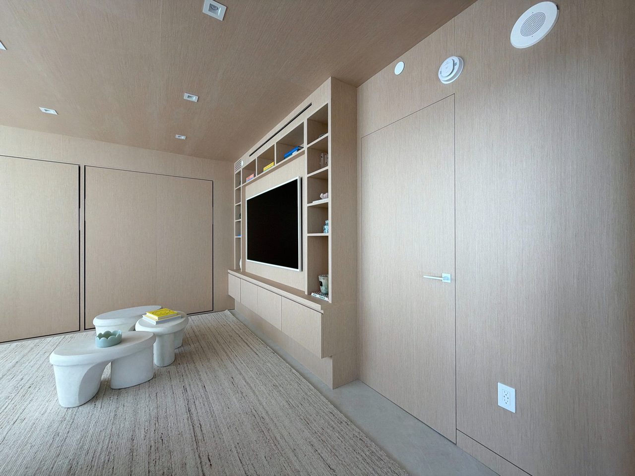 Custom-stained wood veneer media built-in with a recessed TV, open cubby shelving, a floating drawer base, and full-height flush wall paneling alongside