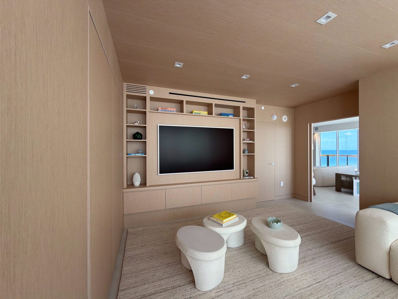 Custom-stained wood veneer TV built-in beside a doorway to an ocean-view living room, with open cubbies and a floating drawer base