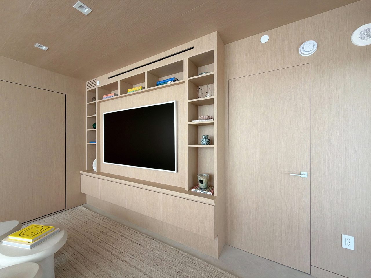 Custom-stained wood veneer TV built-in with a white-framed recessed screen, open display cubbies, and a push-latch credenza base