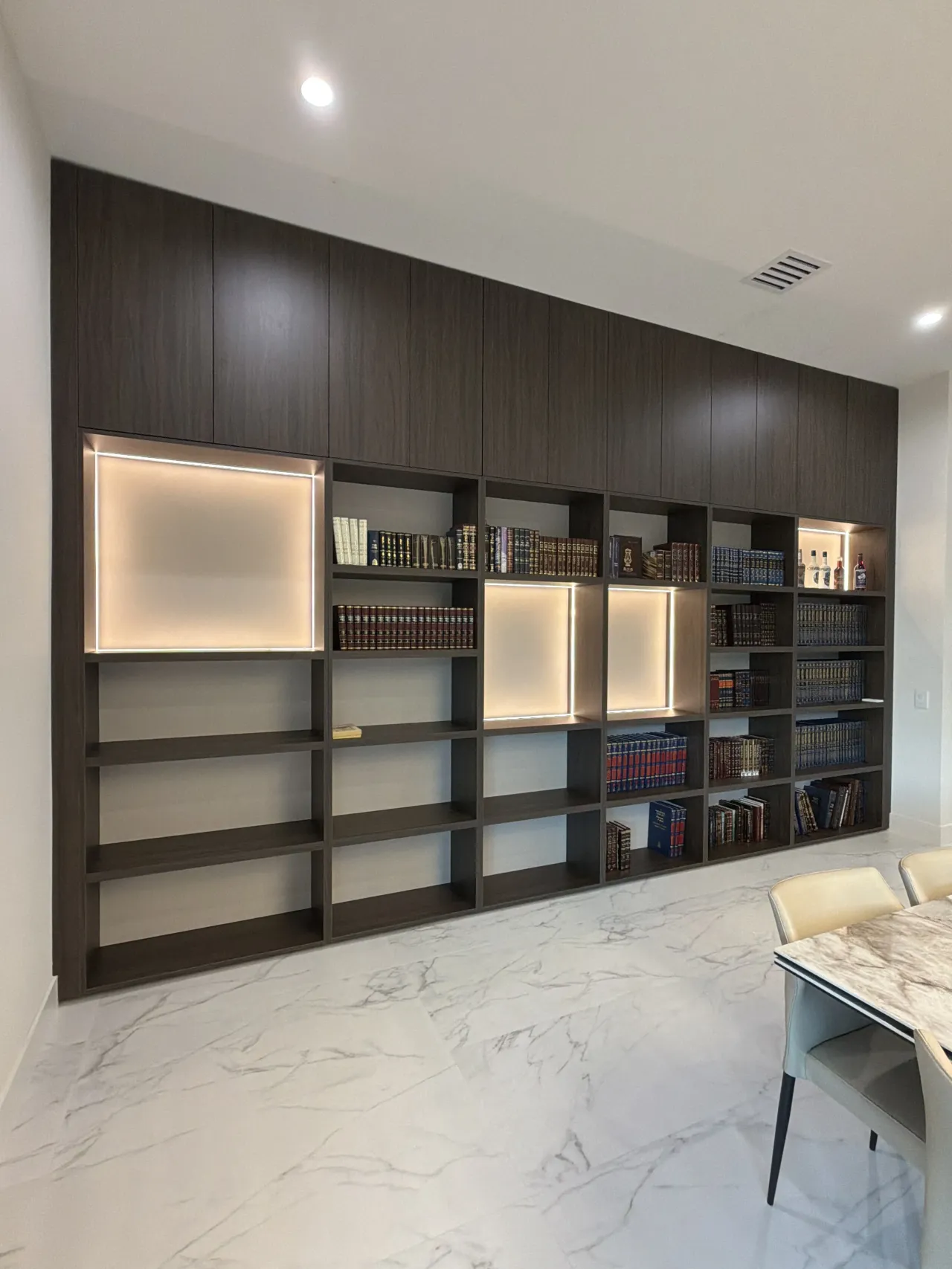 Dark espresso wood-grain melamine library wall with backlit square niches, open book shelving, and veined stone floor