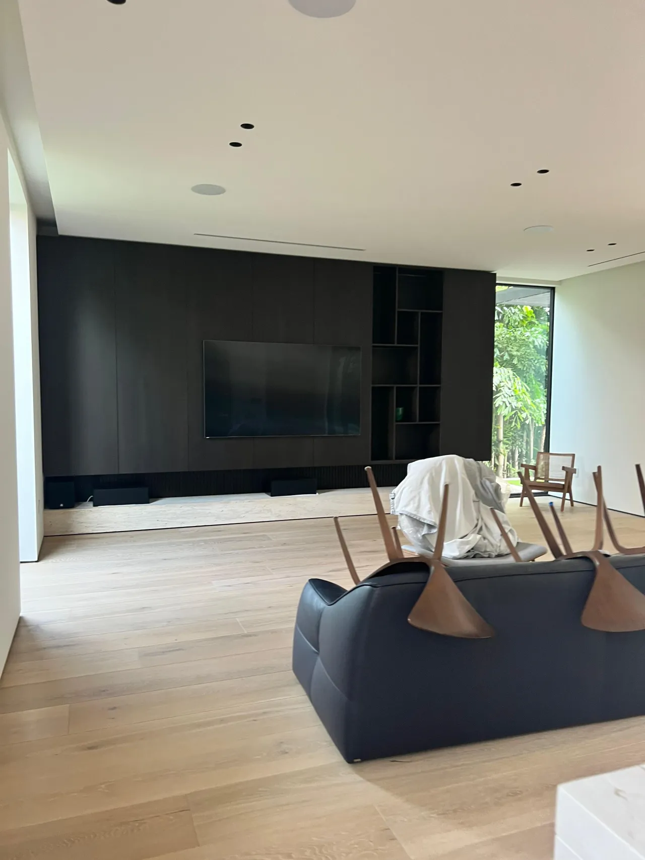 Dark flat-panel media wall with wall-mounted TV and an asymmetric open grid of shelf cutouts at one end, wood plank floor and dark sofa in front