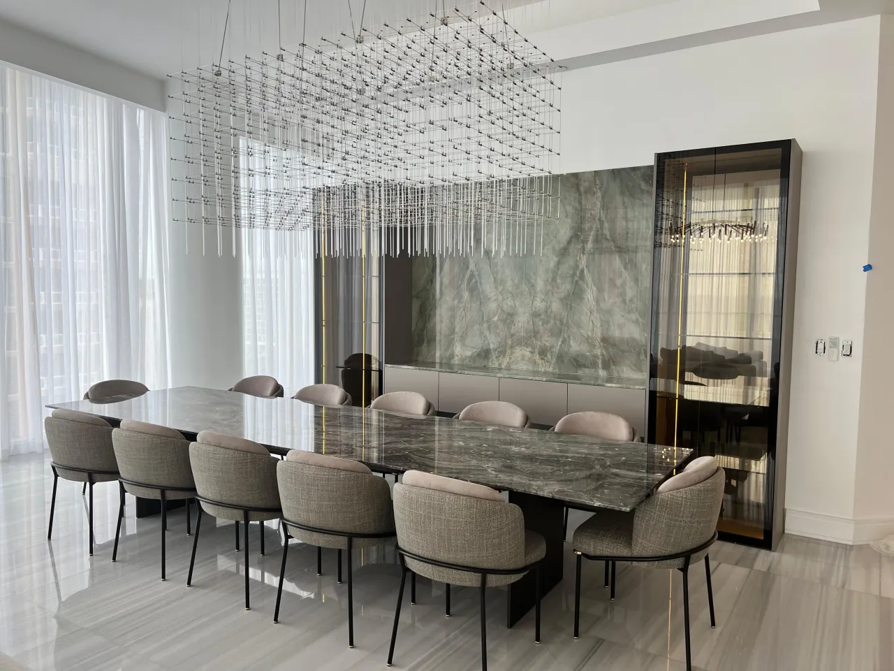 Dining room with a cubed crystal chandelier, veined stone accent wall, and a black glass display cabinet with mirrored shelves