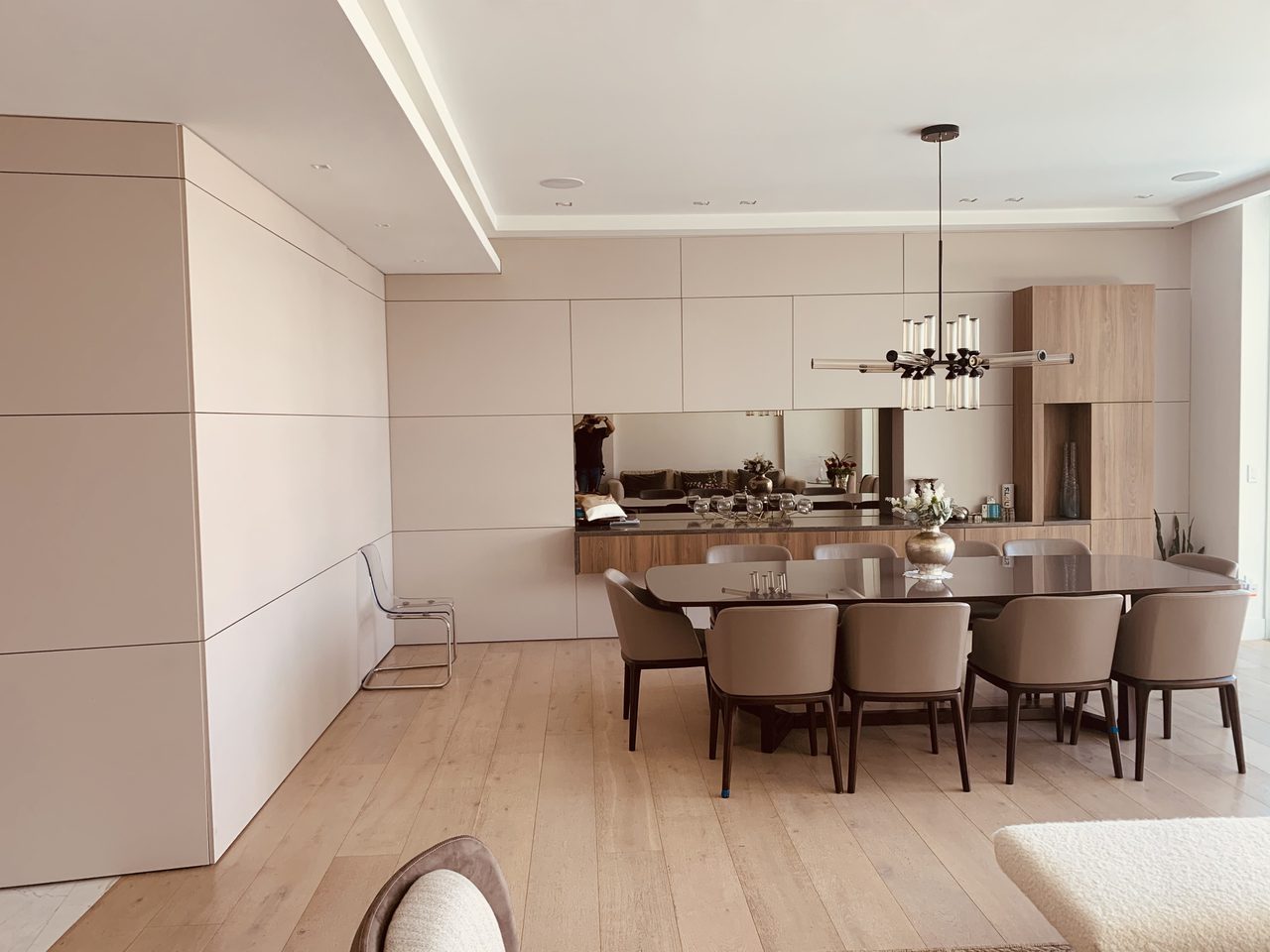 Dining area with floor-to-ceiling cream flat-panel cabinetry, a mirrored niche, wood-grain tall cabinet, and an oval table with upholstered chairs
