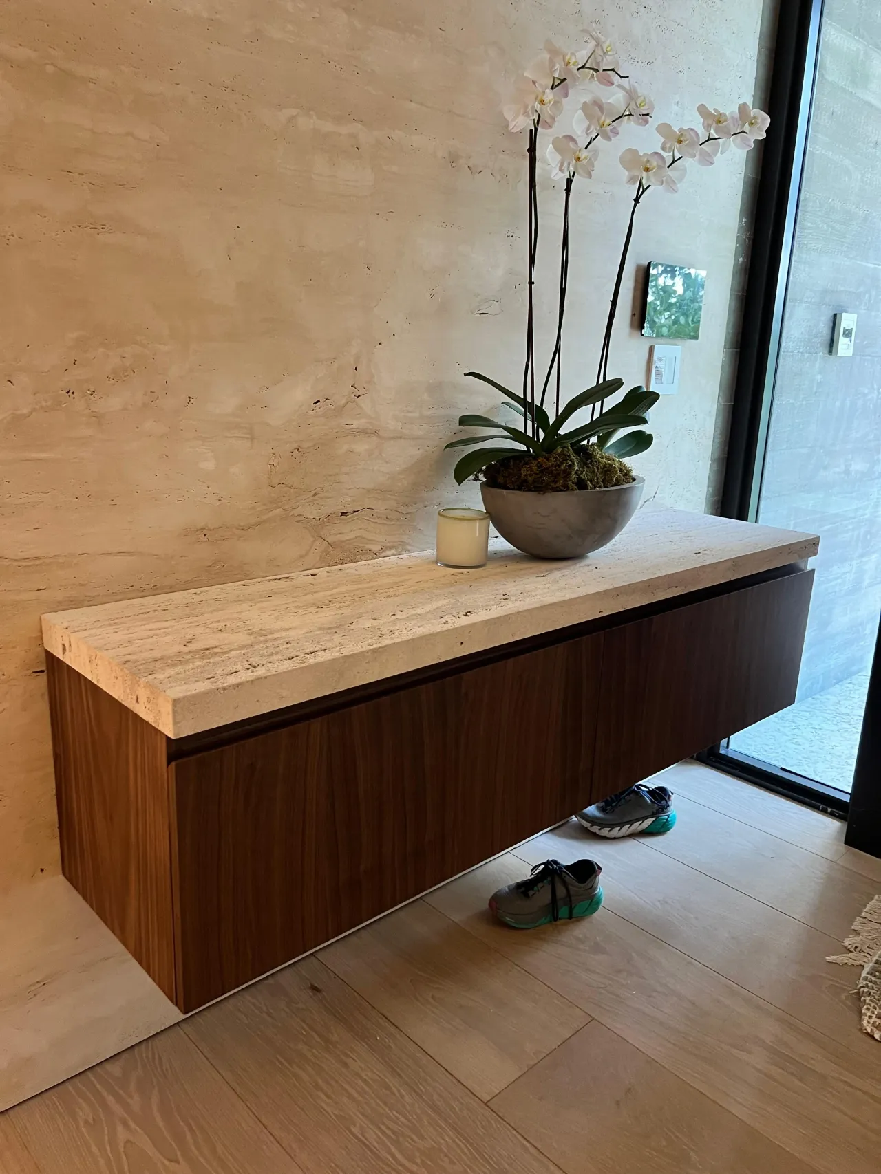 Floating dark wood console with stone top and orchid plant against a stone-clad wall, glass balcony door to the side