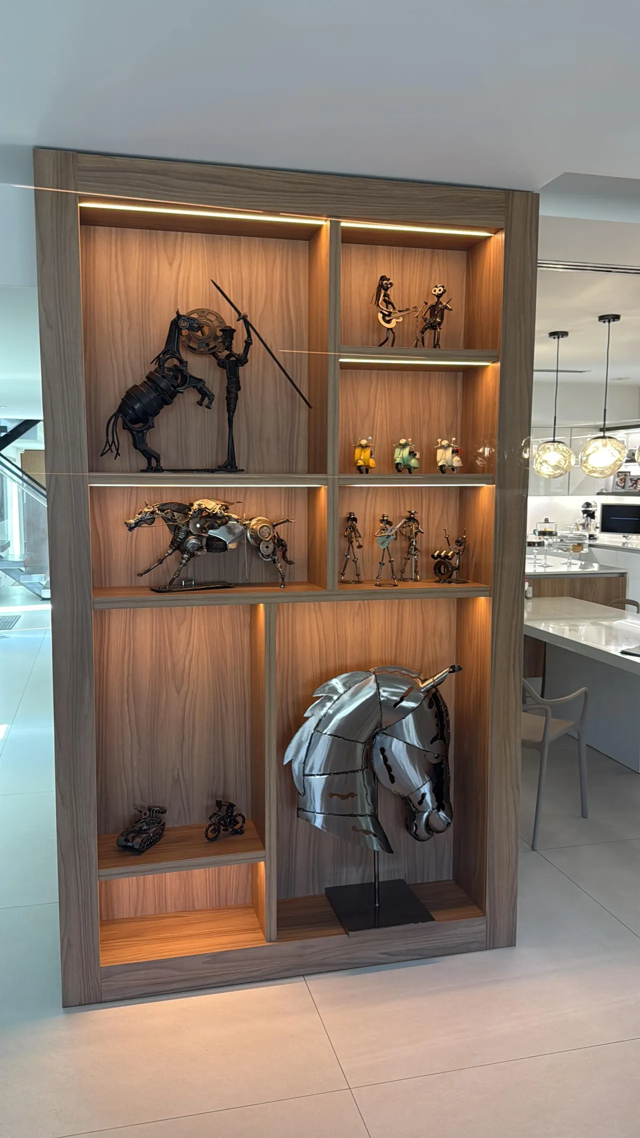 Illuminated open display shelf unit holding collectible metal art sculptures (horses, figures) built into a wood-tone wall