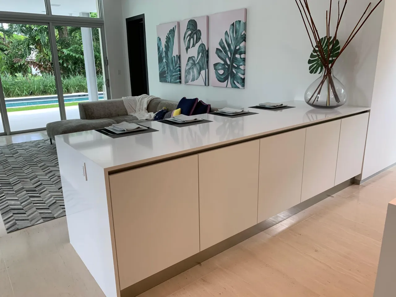 Long island with a white stone-look top and cream flat-panel fronts, glass vase of branches on top, three leaf prints on the wall behind