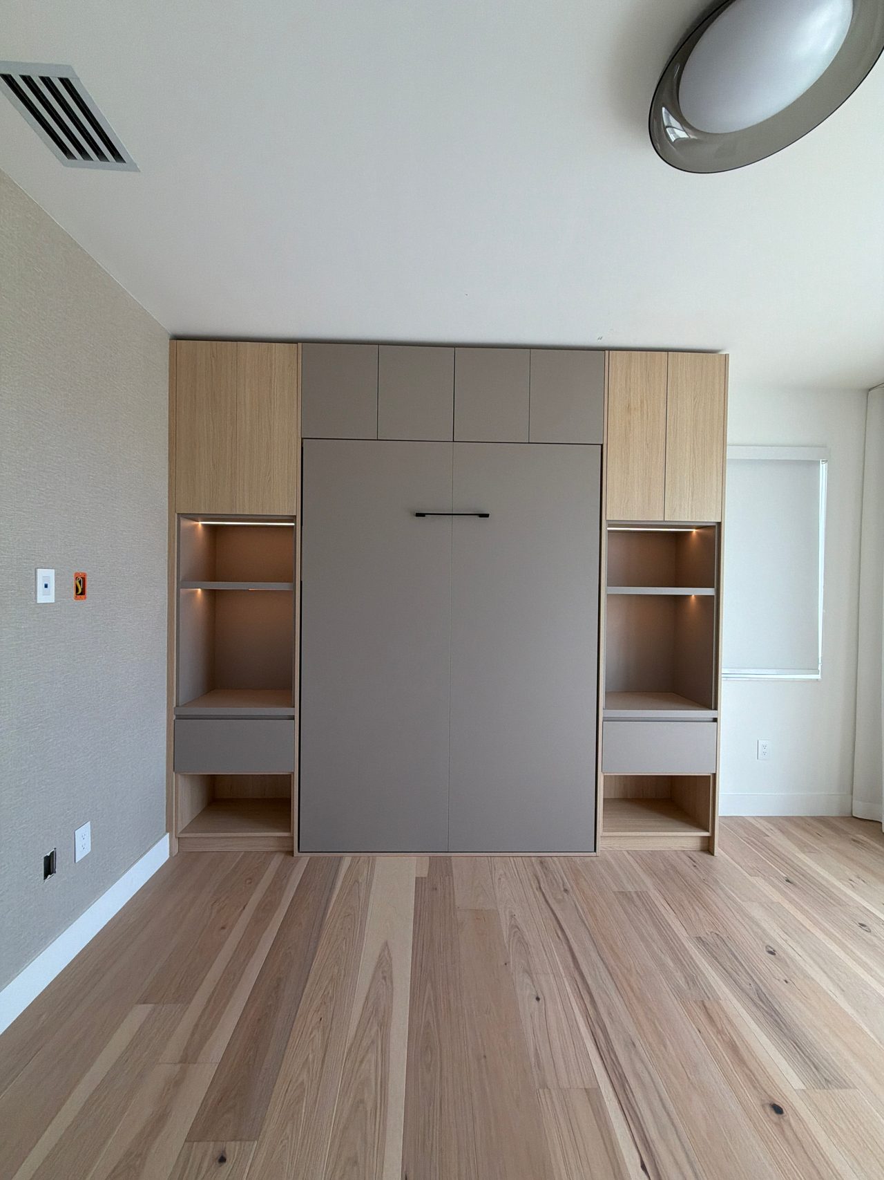 Light wood-grain melamine and gray built-in wall unit with a fold-down murphy bed panel and cubby shelving above and below