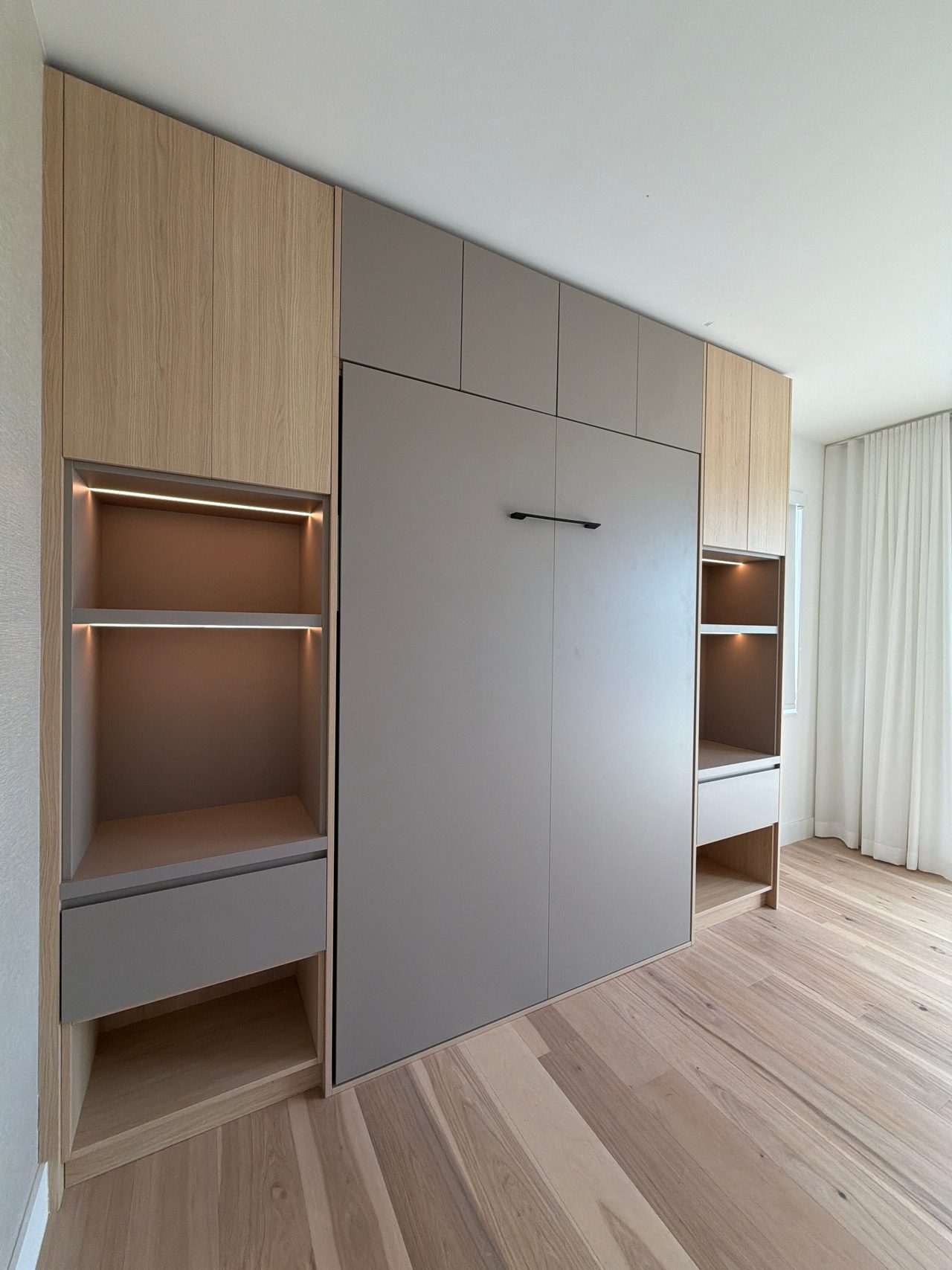 Light wood-grain melamine and gray murphy bed wall unit from a different rotated angle with cubby shelving