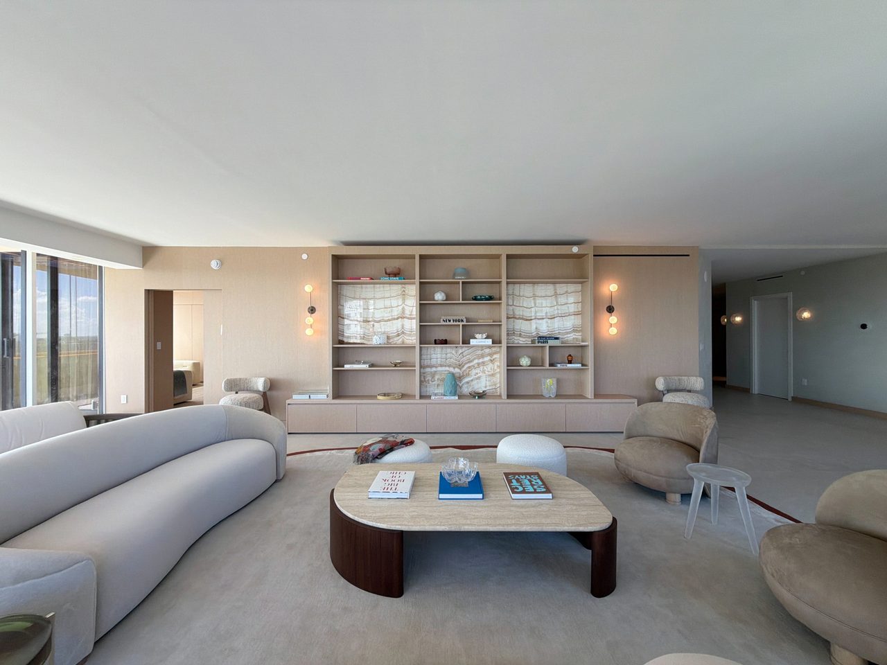 Living room custom-stained wood veneer built-in with open shelving, backlit veined-stone panels, and a push-latch credenza base, opening to the kitchen