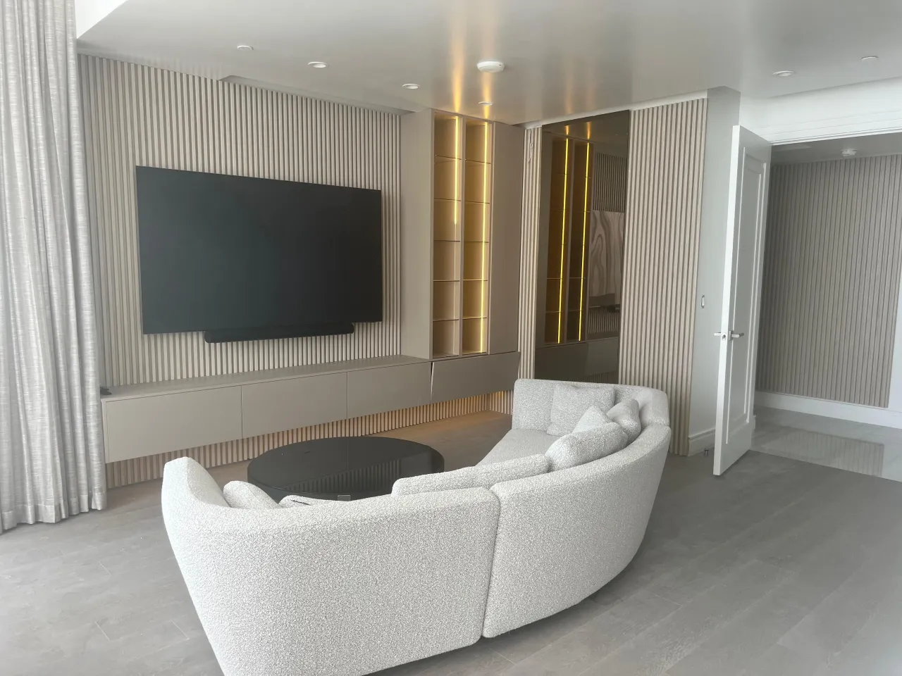 Living room with vertical fluted wall paneling, mounted TV, gold-lit vertical accent strips, and a curved boucle sofa