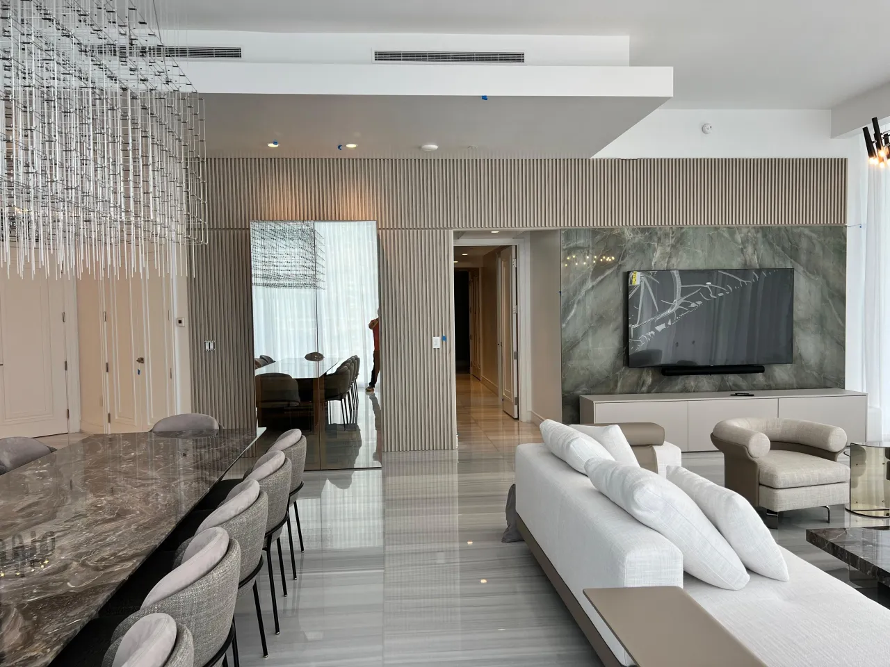 Living area with vertical fluted wall paneling, a green veined stone wall behind a mounted TV over a low cabinet, and a mirrored door panel