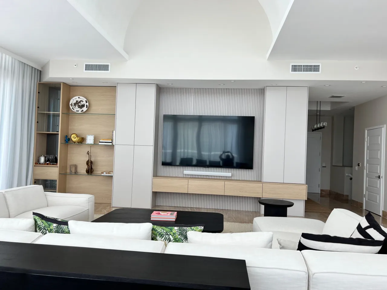 Living room with wall-mounted TV on a fluted vertical panel accent, floating light wood console below, flanked by white cabinet towers, vaulted ceiling