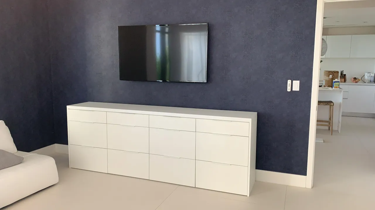 Navy textured accent wall with wall-mounted TV above a long white drawer unit with flat fronts, white sofa at left and tile floor