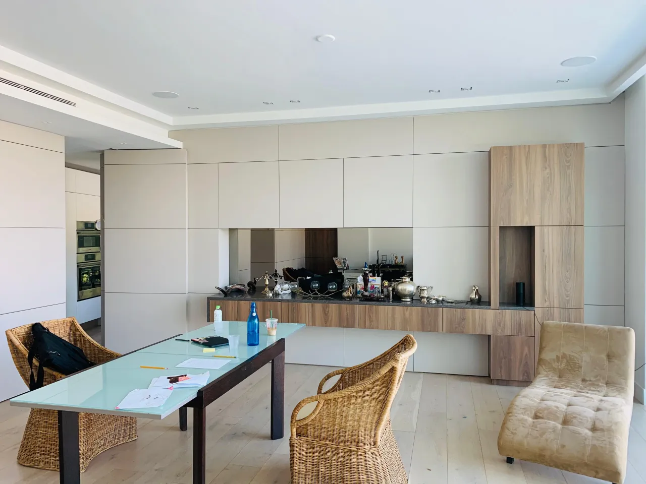 Open-plan dining/kitchen with full-wall cream cabinetry, dark stone countertop with mirror backsplash, and a wood-tone tall accent cabinet at the end