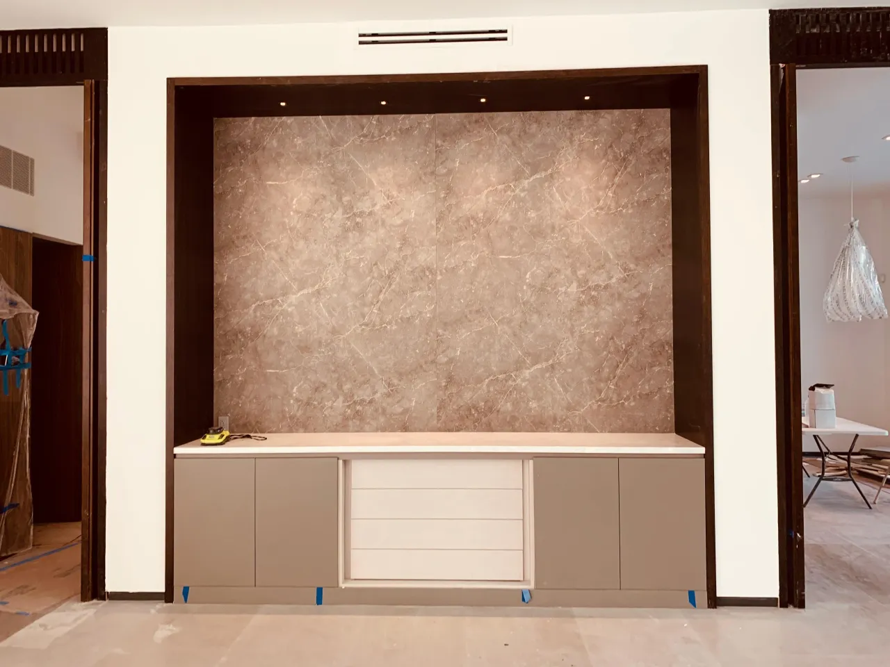 Recessed wall niche in pinkish-brown veined stone above a base cabinet with taupe doors and a light central drawer stack
