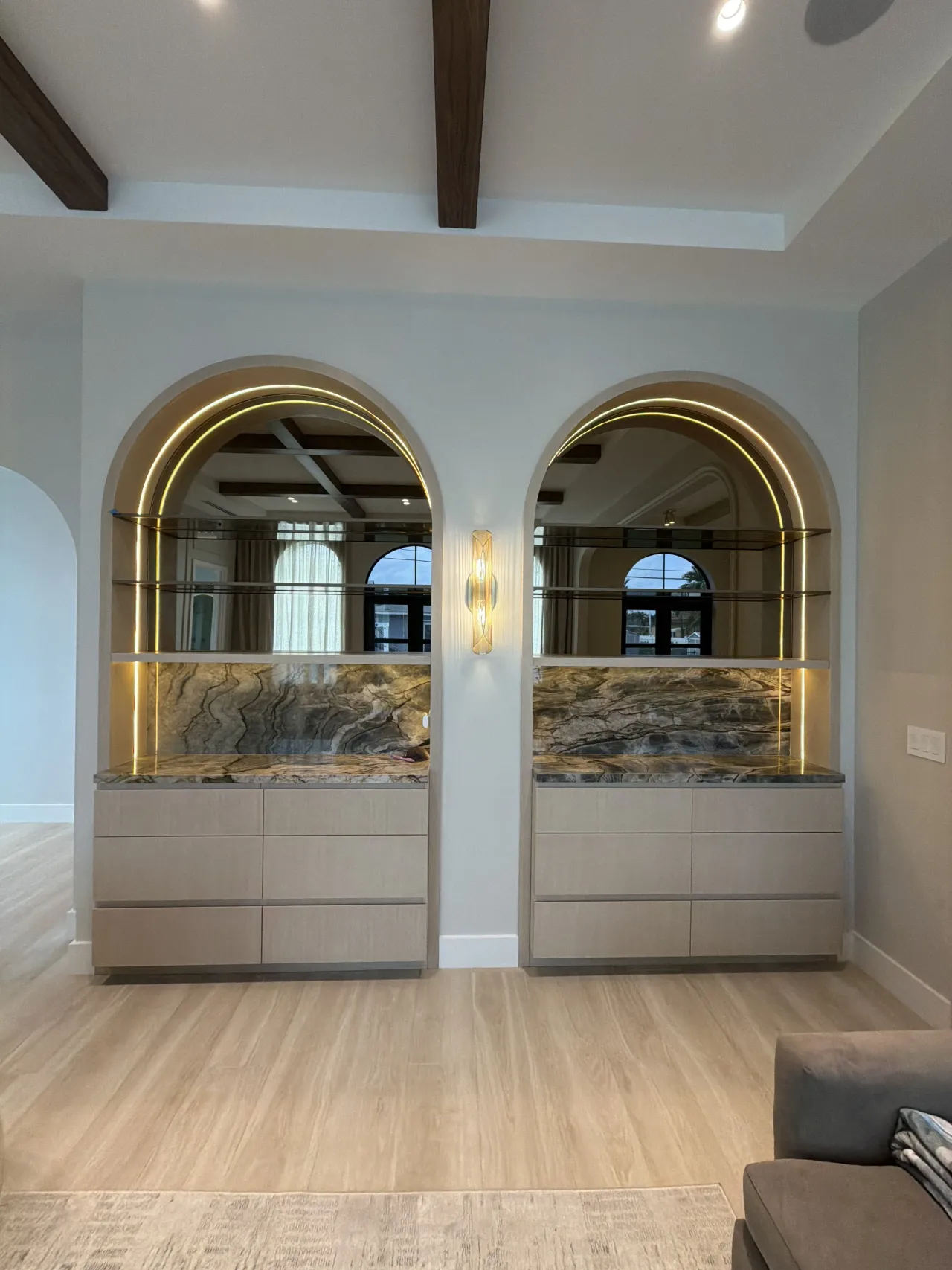 Two side-by-side arched display units with stone-look backsplash, glass shelves, and gold LED trim over wood-grain melamine drawer bases