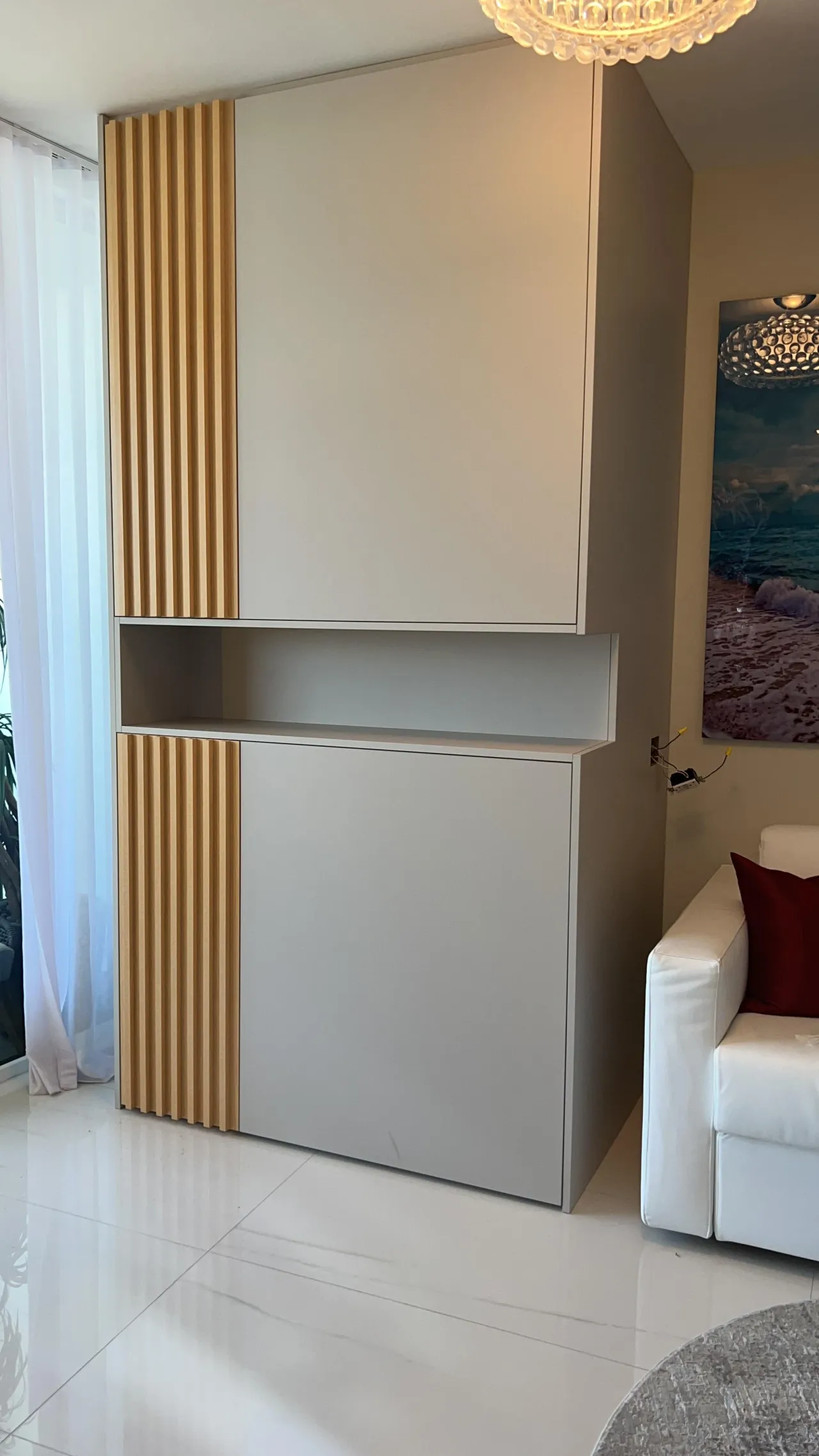 Tall two-door cabinet in gray with vertical light wood-grain slat stripes and an open middle shelf niche, beside sheer curtains on a glossy tile floor