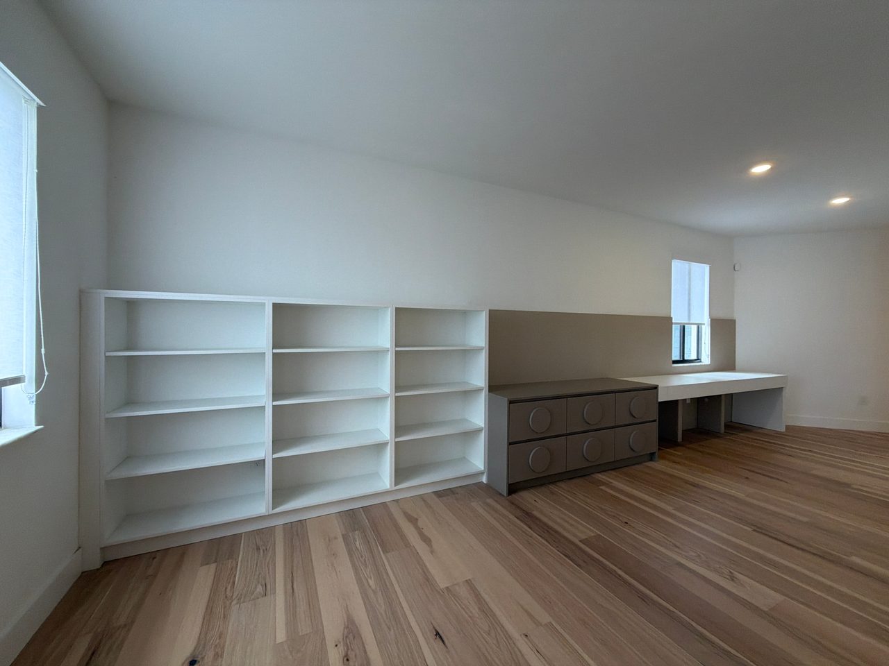 Taupe built-in dresser with large circular door pulls beside a white open bookshelf