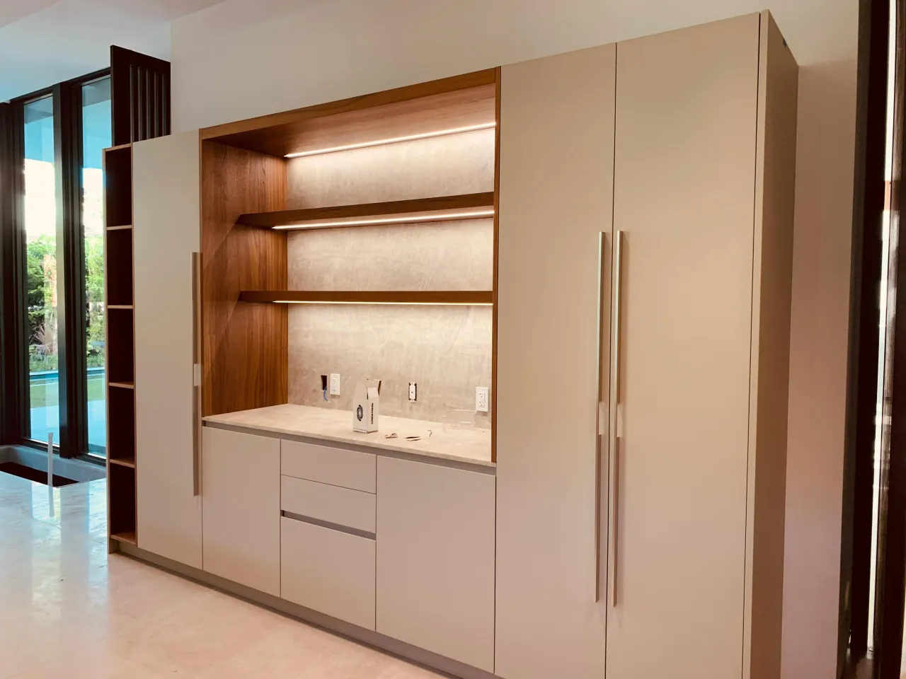 Taupe flat-panel cabinetry with a wood-lined nook, light stone counter, and two floating shelves lit by LED strips, tall doors with long handles
