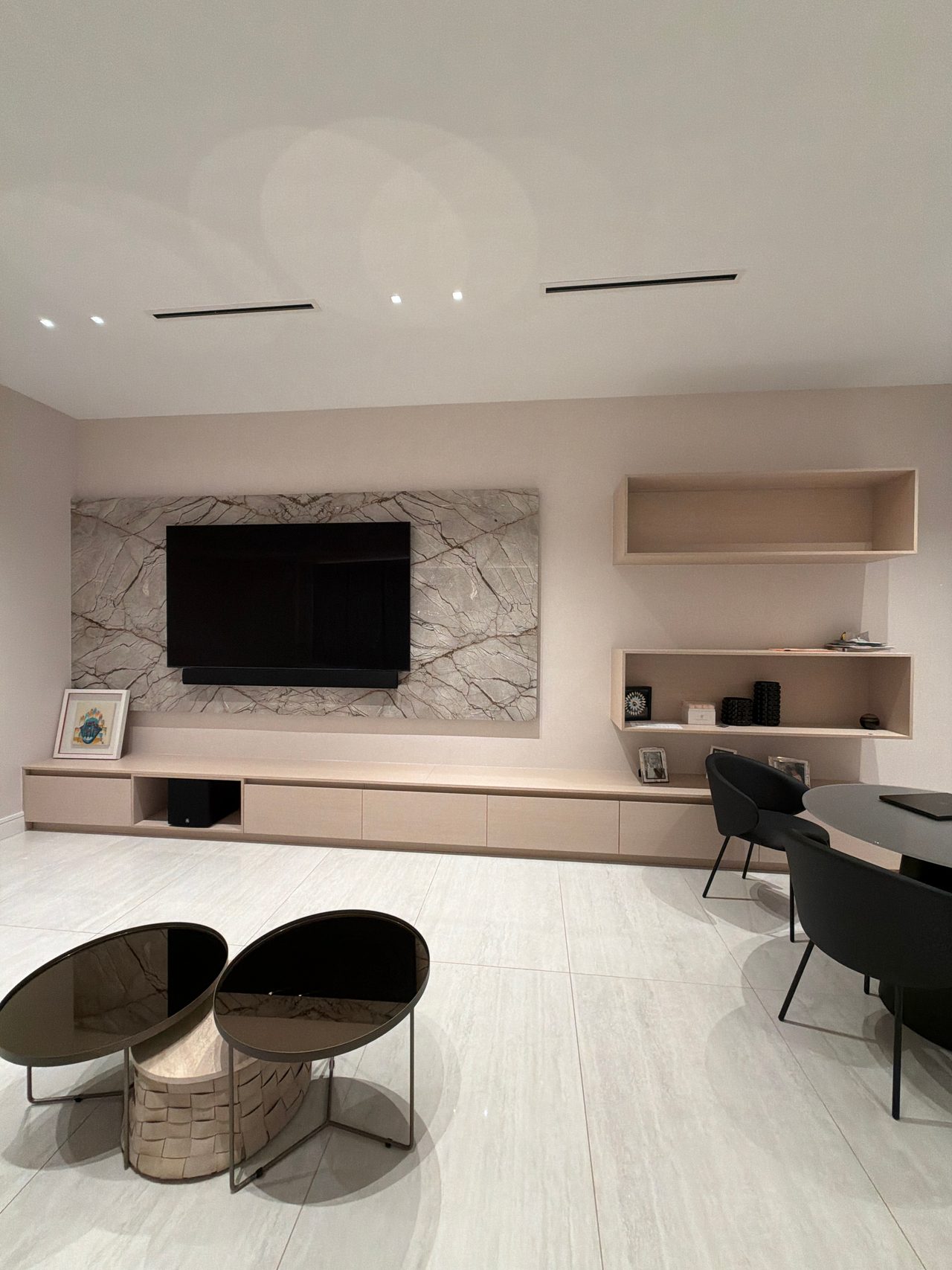 Veined stone wall behind a mounted TV above a long low wood-grain credenza, with two open wood-grain shelf boxes on the wall to the right